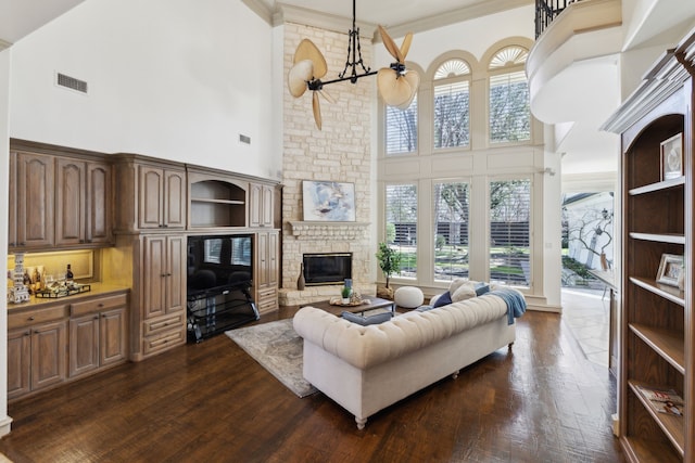 living area featuring dark wood-type flooring, crown molding, visible vents, and a large fireplace