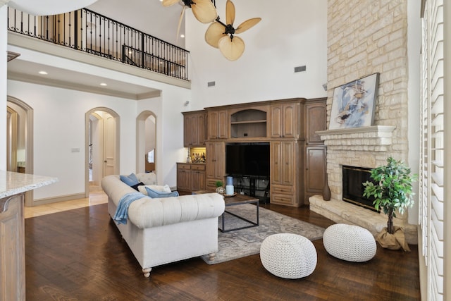 living area featuring arched walkways, a fireplace, a ceiling fan, and wood finished floors