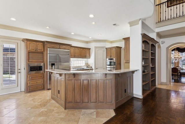 kitchen featuring light stone counters, built in appliances, and crown molding