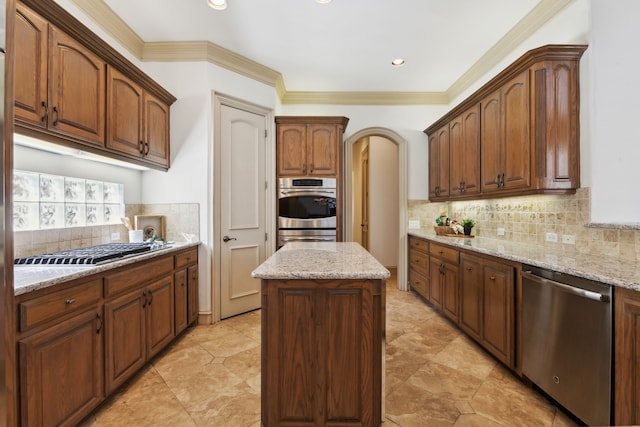 kitchen featuring light stone countertops, a kitchen island, ornamental molding, decorative backsplash, and appliances with stainless steel finishes