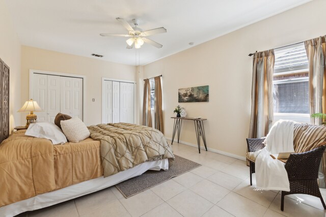 bedroom featuring light tile patterned flooring, visible vents, baseboards, and multiple closets