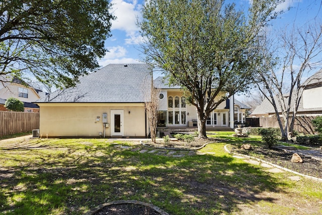 back of house featuring stucco siding, a yard, fence, and a shingled roof