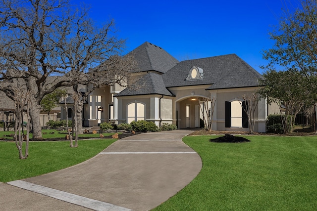 french country inspired facade featuring stucco siding, driveway, and a front lawn