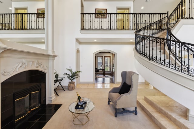 tiled living area with arched walkways, baseboards, a towering ceiling, stairs, and a tile fireplace