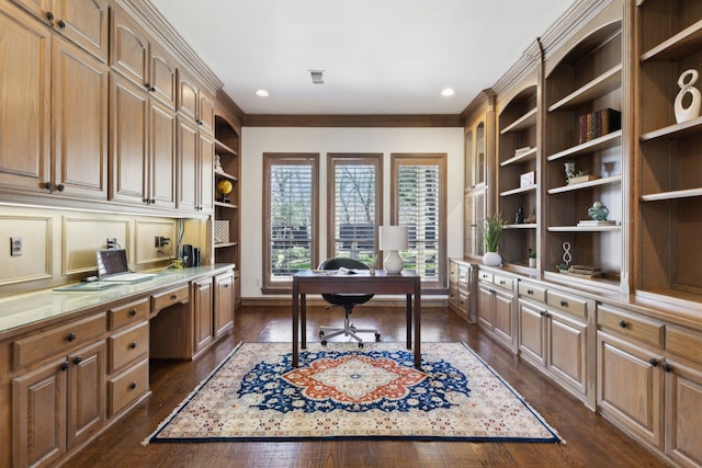 office area with visible vents, built in shelves, ornamental molding, built in desk, and dark wood-style flooring