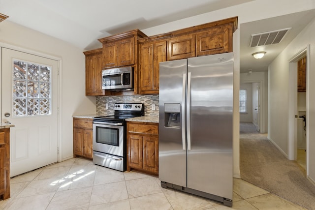 kitchen featuring visible vents, light tile patterned flooring, stainless steel appliances, tasteful backsplash, and brown cabinets