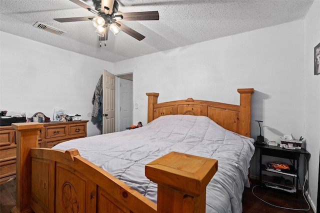 bedroom with a ceiling fan, wood finished floors, visible vents, and a textured ceiling