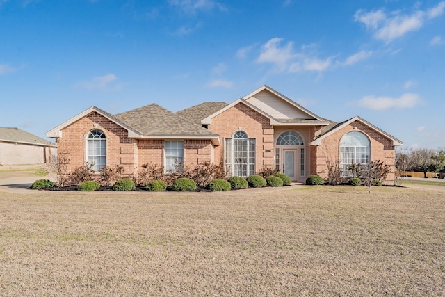 ranch-style home featuring a front yard, brick siding, and a shingled roof