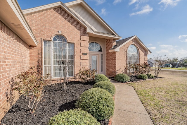 doorway to property featuring brick siding and a lawn