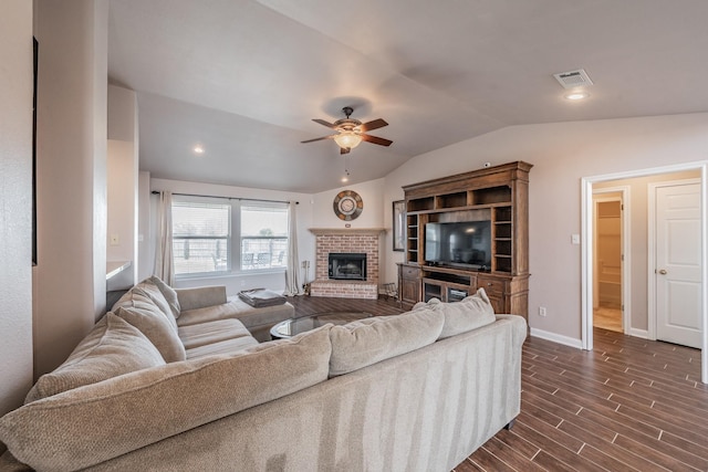 living area featuring a ceiling fan, visible vents, dark wood-type flooring, vaulted ceiling, and a brick fireplace