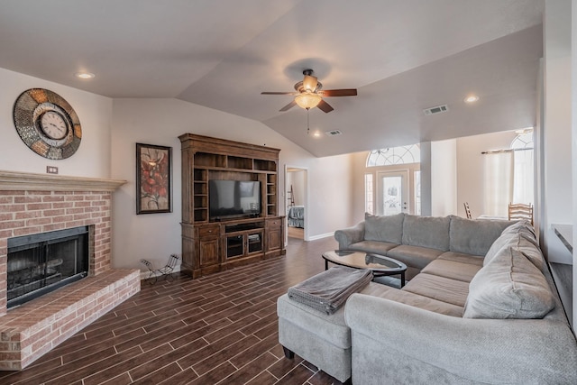 living room with visible vents, lofted ceiling, a brick fireplace, ceiling fan, and dark wood-style flooring