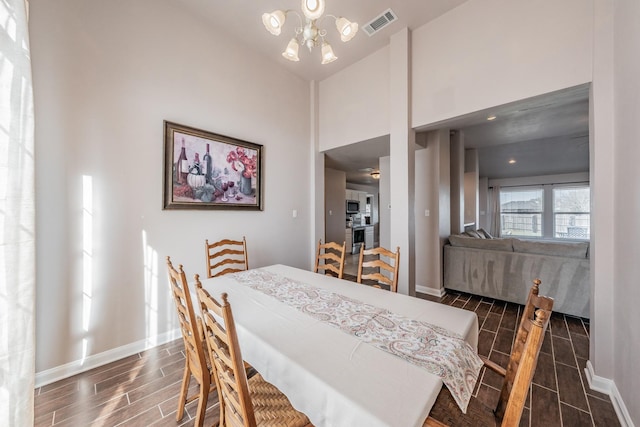 dining space with visible vents, a notable chandelier, a high ceiling, baseboards, and wood tiled floor