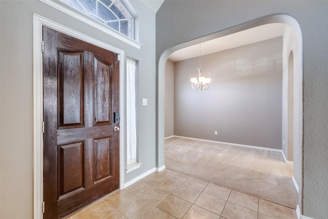 foyer featuring arched walkways, light tile patterned floors, light colored carpet, and a notable chandelier