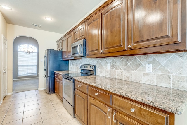 kitchen featuring light stone countertops, visible vents, light tile patterned flooring, arched walkways, and appliances with stainless steel finishes