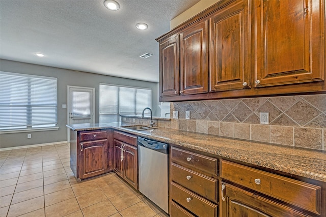 kitchen with light tile patterned floors, a peninsula, a sink, stainless steel dishwasher, and backsplash