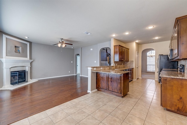 kitchen with arched walkways, a fireplace with raised hearth, and light stone countertops