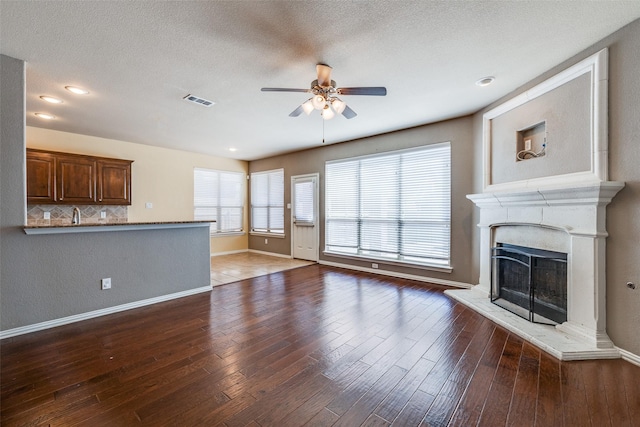 unfurnished living room with visible vents, a fireplace with raised hearth, ceiling fan, and hardwood / wood-style flooring