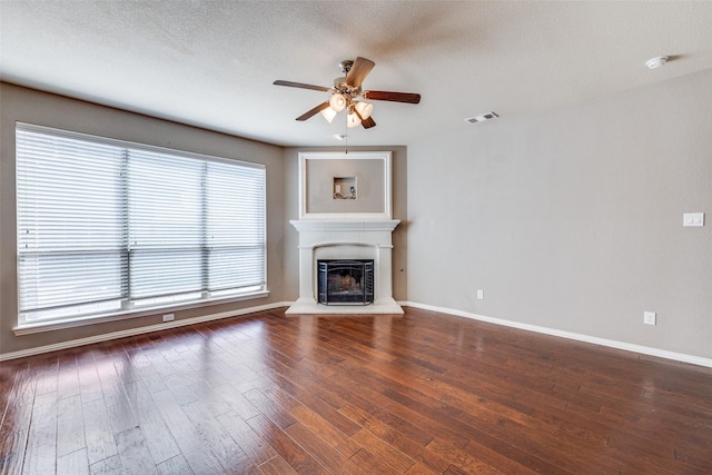 unfurnished living room with visible vents, a fireplace with raised hearth, a ceiling fan, baseboards, and dark wood-style flooring