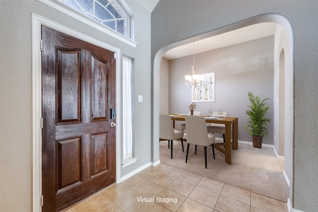 entryway with light tile patterned floors, a notable chandelier, arched walkways, and light colored carpet