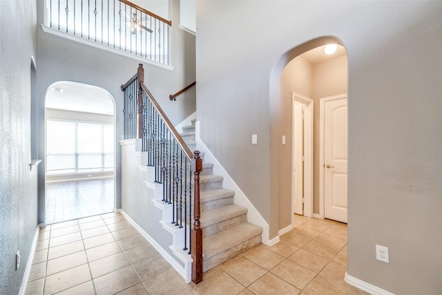 stairs featuring arched walkways, tile patterned flooring, baseboards, and a towering ceiling