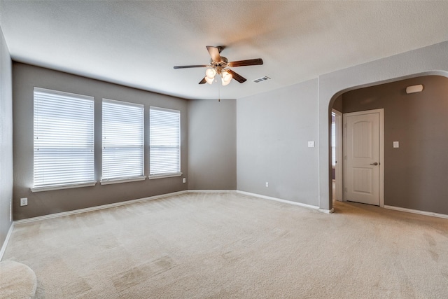 unfurnished room featuring visible vents, baseboards, arched walkways, ceiling fan, and light colored carpet