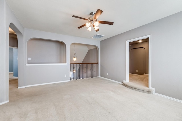 carpeted empty room featuring visible vents, arched walkways, baseboards, and a ceiling fan