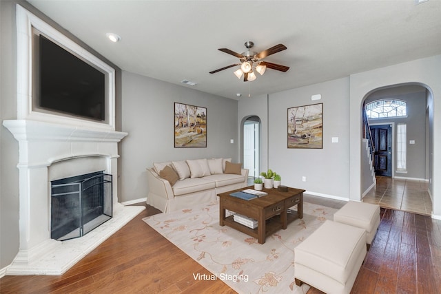 living area featuring arched walkways, visible vents, a fireplace with raised hearth, and wood-type flooring