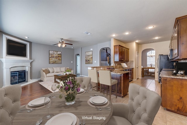 dining space featuring a glass covered fireplace, recessed lighting, arched walkways, light tile patterned floors, and ceiling fan