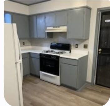 kitchen featuring range with gas cooktop, under cabinet range hood, light countertops, gray cabinets, and freestanding refrigerator