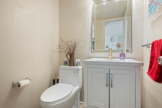 half bathroom featuring toilet, vanity, and a textured wall