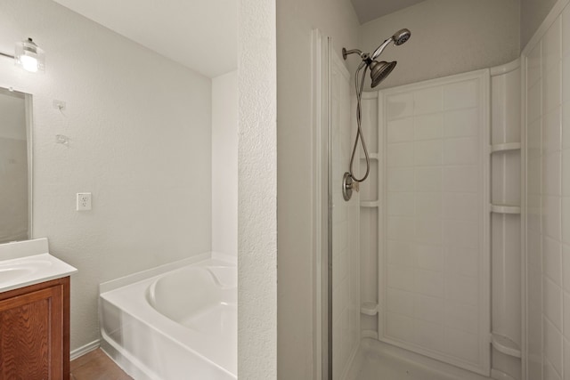 full bath featuring a bath, vanity, a shower, and a textured wall