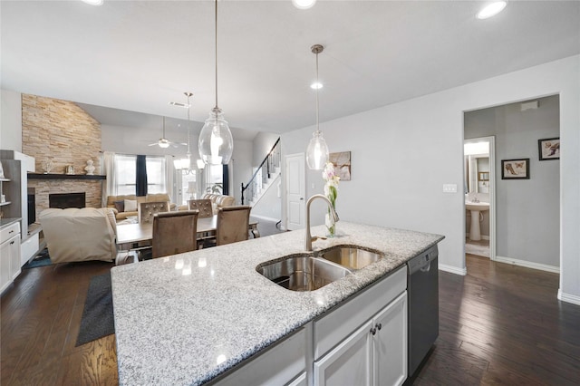 kitchen featuring stainless steel dishwasher, dark wood-type flooring, a fireplace, and a sink