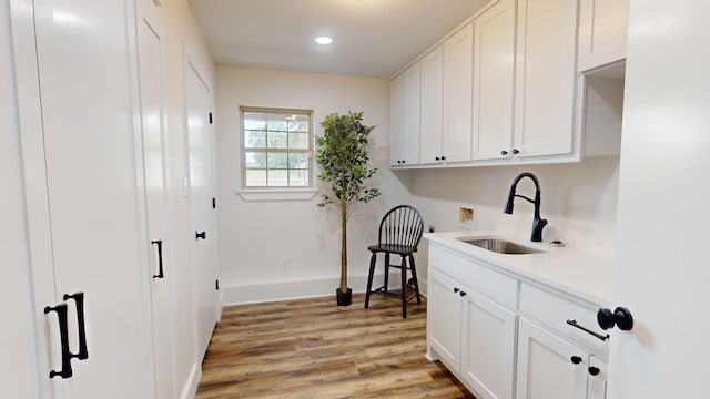 laundry room featuring baseboards, hookup for a washing machine, light wood-style flooring, cabinet space, and a sink