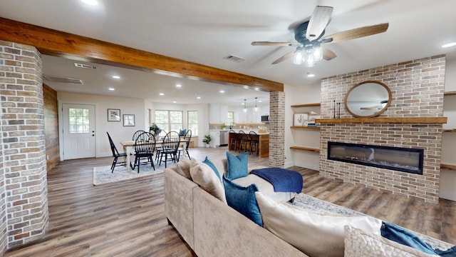 living area with visible vents, beamed ceiling, a glass covered fireplace, and wood finished floors