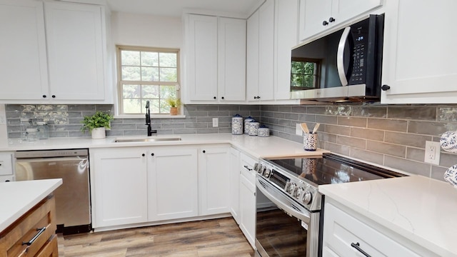 kitchen featuring backsplash, light wood-type flooring, white cabinets, stainless steel appliances, and a sink