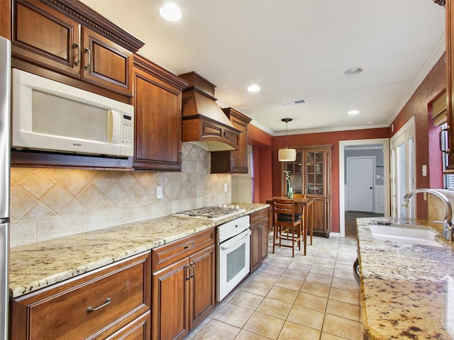 kitchen featuring visible vents, crown molding, premium range hood, white appliances, and a sink