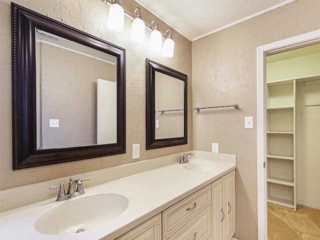 full bathroom with double vanity, ornamental molding, a textured wall, and a sink