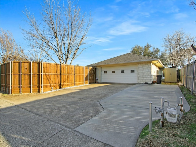 view of side of home with brick siding, an attached garage, fence, an outbuilding, and driveway