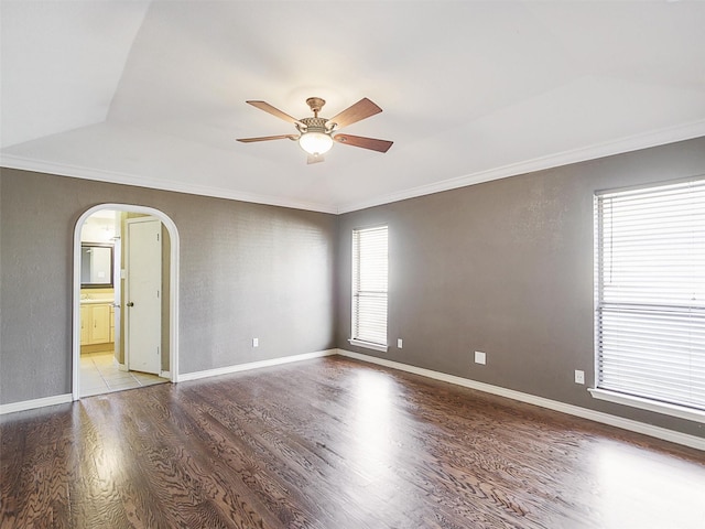 spare room with crown molding, baseboards, wood finished floors, arched walkways, and a ceiling fan