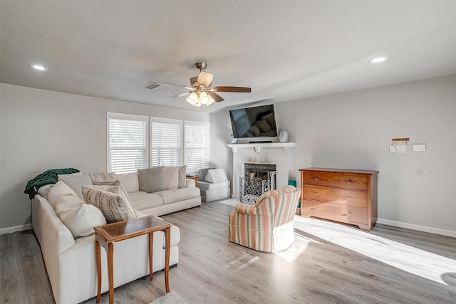 living area featuring a fireplace, wood finished floors, a ceiling fan, and baseboards