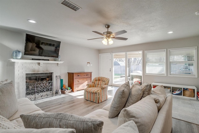 living area with visible vents, a brick fireplace, ceiling fan, wood finished floors, and a textured ceiling