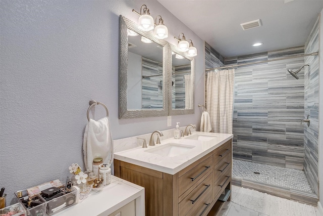 bathroom with a sink, visible vents, double vanity, and a tile shower