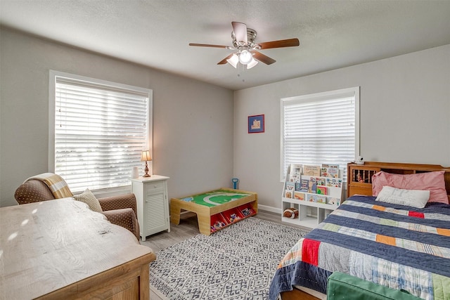 bedroom featuring a ceiling fan, baseboards, light wood finished floors, and a textured ceiling