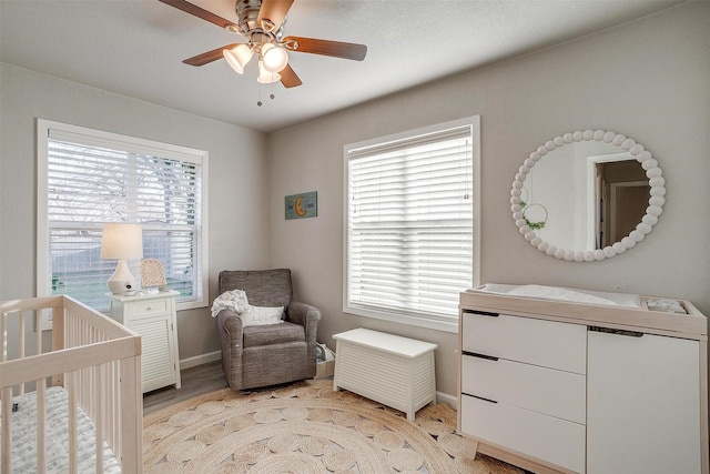 bedroom with baseboards, light wood-style floors, a crib, and a ceiling fan