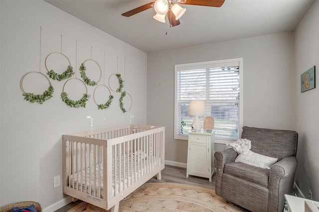 bedroom with ceiling fan, baseboards, a nursery area, and wood finished floors