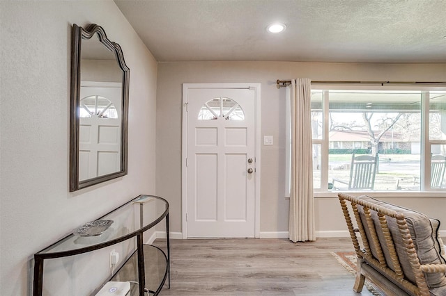 foyer with baseboards, plenty of natural light, a textured ceiling, and light wood-style flooring