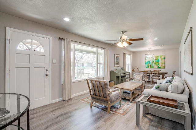 living area with a ceiling fan, baseboards, light wood finished floors, and a textured ceiling