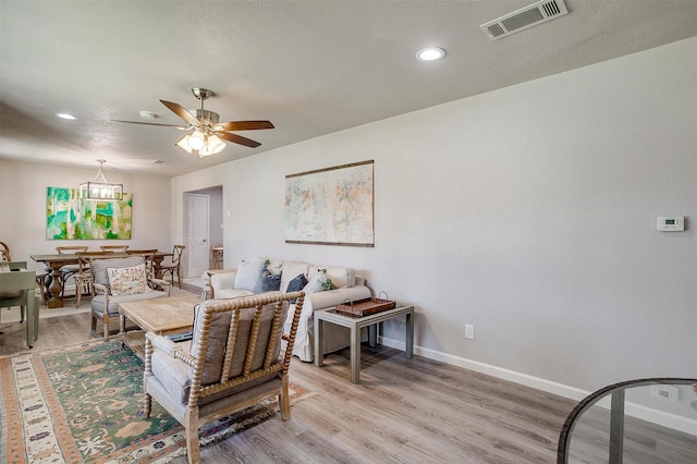 living room featuring light wood finished floors, visible vents, ceiling fan, and baseboards