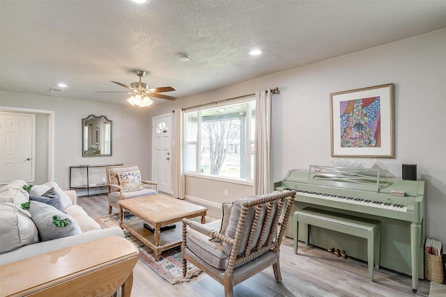 living room featuring a ceiling fan, a textured ceiling, recessed lighting, light wood finished floors, and baseboards