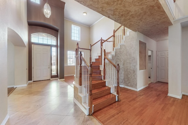 entryway with stairway, baseboards, light wood-style floors, and a towering ceiling